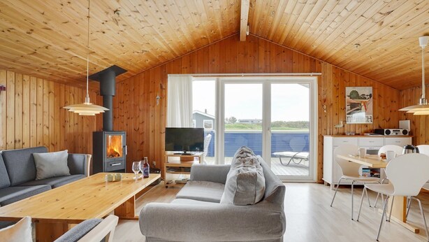Interior acogedor de una cabaña con techo de madera, chimenea, sofá, mesa de comedor y vista a una piscina.