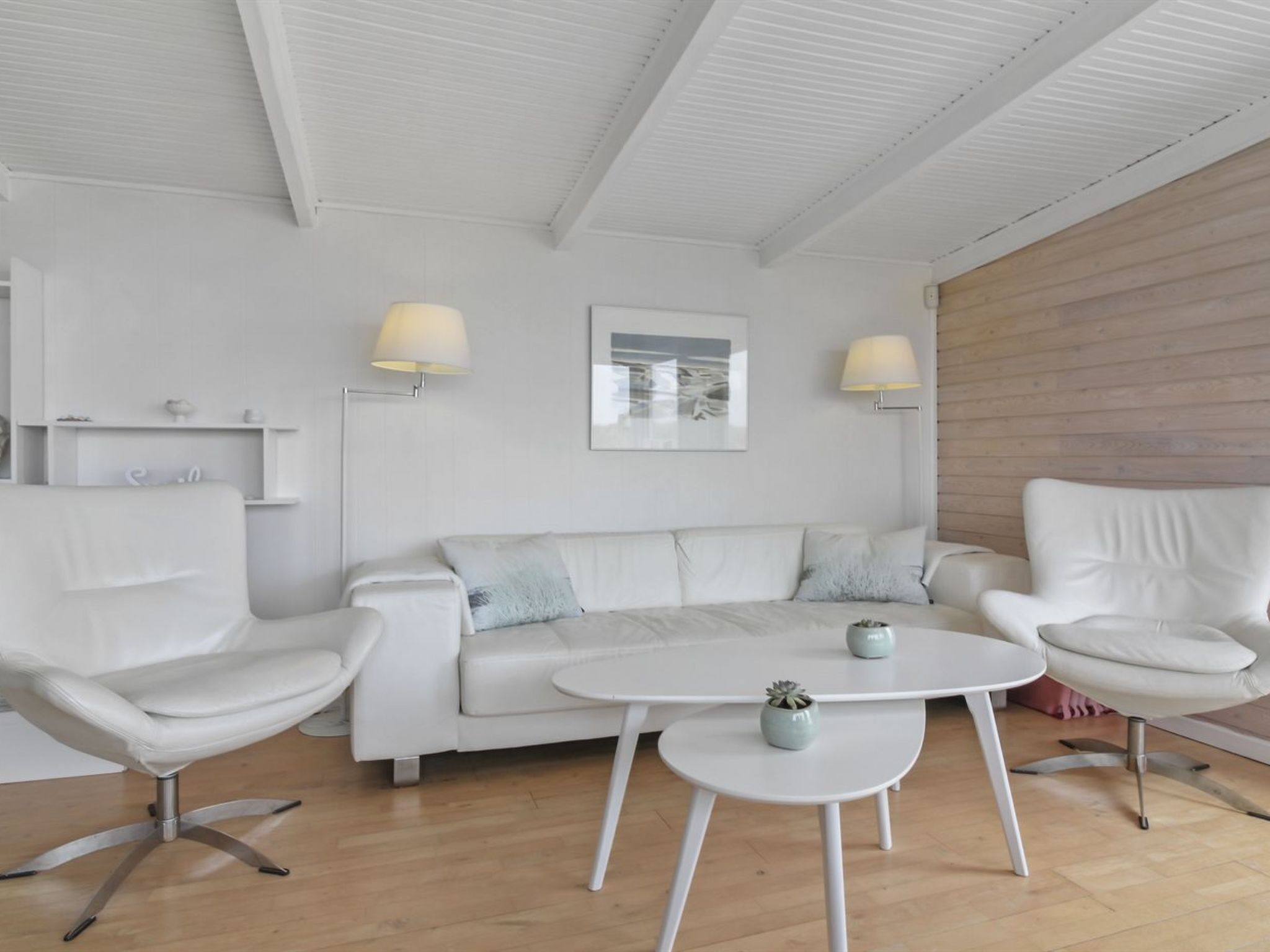A modern living room with a white sofa, two white armchairs, a small white table, and two wall-mounted lamps.