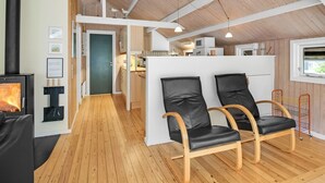 A modern interior with a wood-burning stove, a kitchen area, and two leather chairs.