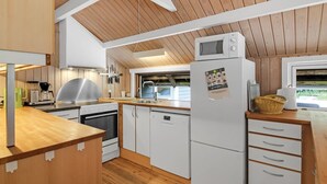 A modern kitchen with wooden ceiling beams, white cabinetry, a built-in oven, a microwave, and a refrigerator.