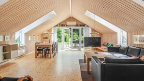 A spacious loft with a high ceiling, wooden beams, a dining area, a living room with a sofa, and a TV.
