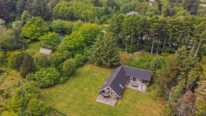 An aerial view of a house surrounded by dense forest, with a well-maintained lawn and a large deck area.