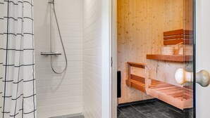 Une salle de bain moderne avec des murs recouverts de carreaux blancs, une douche équipée d’un pommeau flexible et d’un banc en bois.
