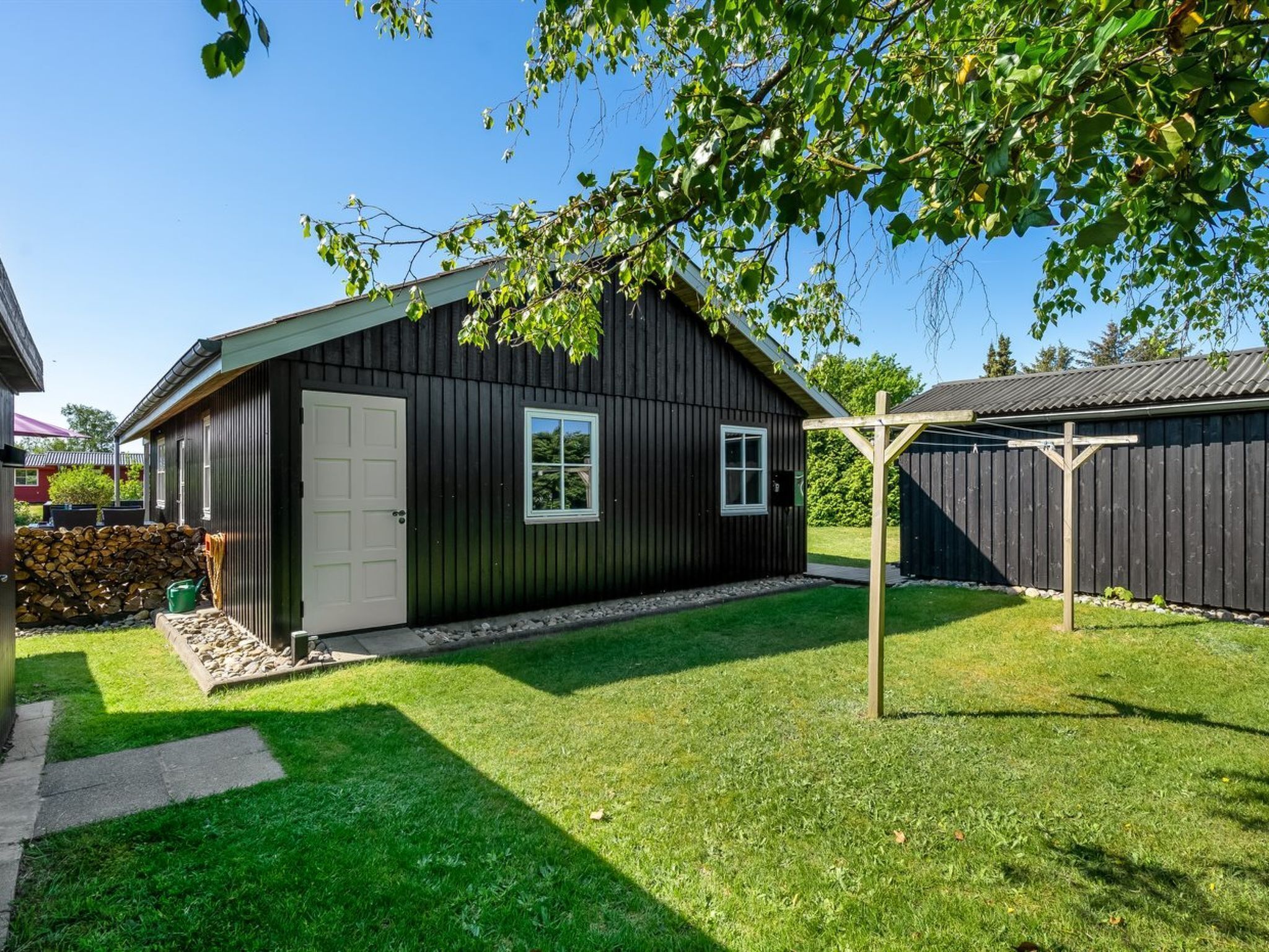 A small, dark wooden building with a white door and windows, surrounded by a well-maintained lawn and a wooden fence.