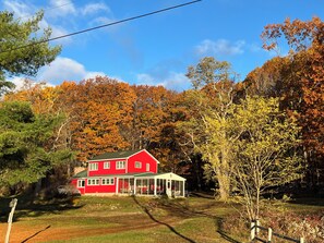 Ein rotes Haus mit einem grünen Dach und einer Veranda, umgeben von Herbstlaub.