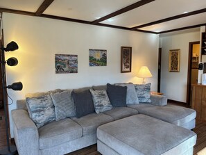 Ein Wohnzimmer mit einem grauen Ecksofa, einer Stehlampe und drei Wandleuchten.