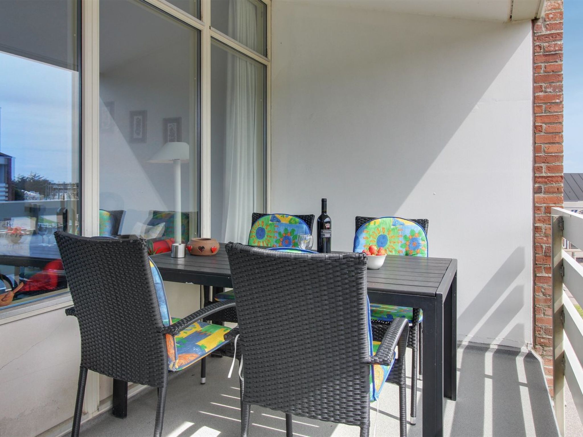 Een balkon met twee rieten stoelen, een tafel en een fles wijn.
