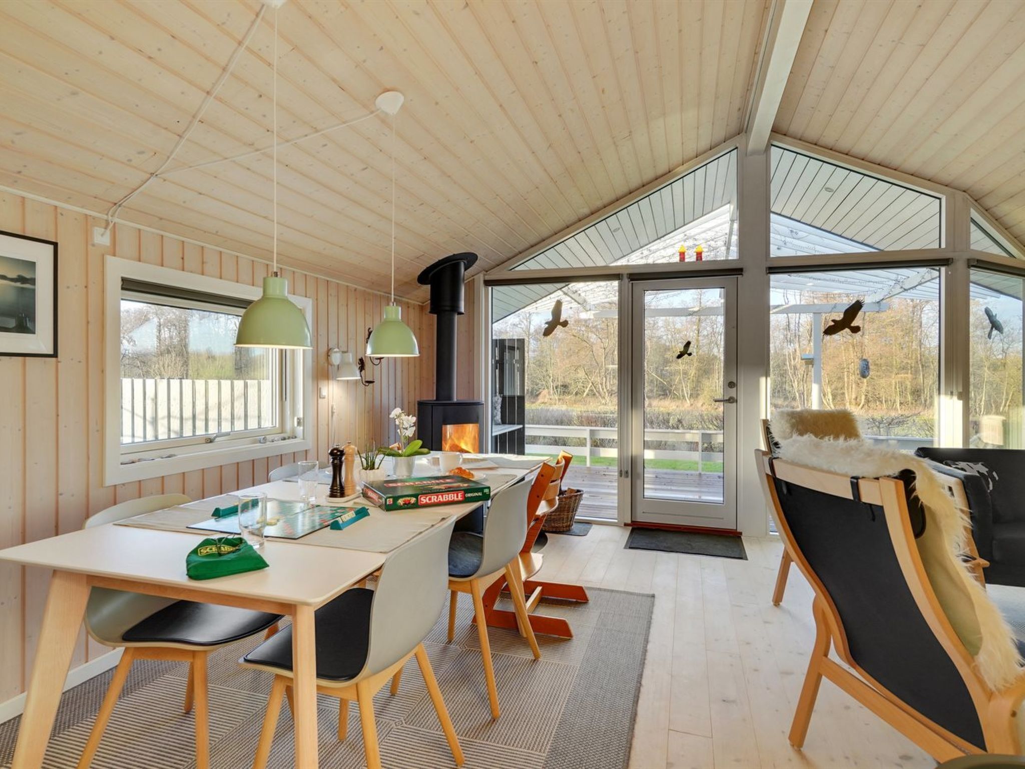 A cozy cabin interior with a dining area, a fireplace, and large windows offering a view of the outdoors.
