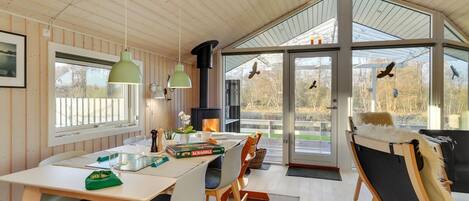 A cozy cabin interior with a dining area, a fireplace, and large windows offering a view of the outdoors.