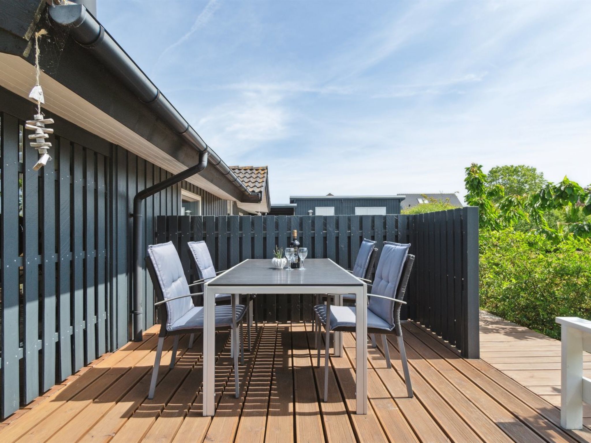 Une terrasse extérieure avec une table et des chaises, une terrasse en bois et une clôture sombre.