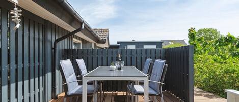 Une terrasse extérieure avec une table et des chaises, une terrasse en bois et une clôture sombre.