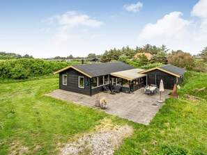 Une maison moderne dotée d’un patio, d’un espace salon extérieur abrité et d’une grande fenêtre donnant sur la verdure environnante.