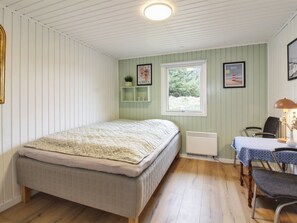 Une chambre comprenant un lit, un bureau, une chaise, un radiateur et une fenêtre donnant sur un espace verdoyant.