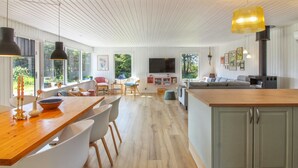 Amplia sala de estar con mesa de comedor de madera, sillas blancas, un sofá y una cocina con una isla grande.