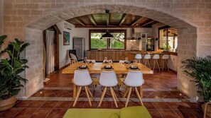 Comedor con una larga mesa de madera dispuesta para seis personas, rodeada de sillas blancas.