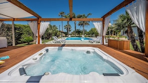 Una terraza de madera con jacuzzi, piscina y sillas de descanso.