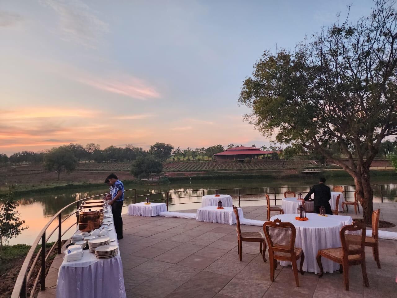 An outdoor dining area with tables set up for guests, overlooking a body of water and a distant building.