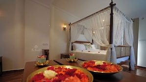 A hotel room with a four-poster bed, a bedside table with a lamp, and a nightstand. - The Hamlet (Kondapur)