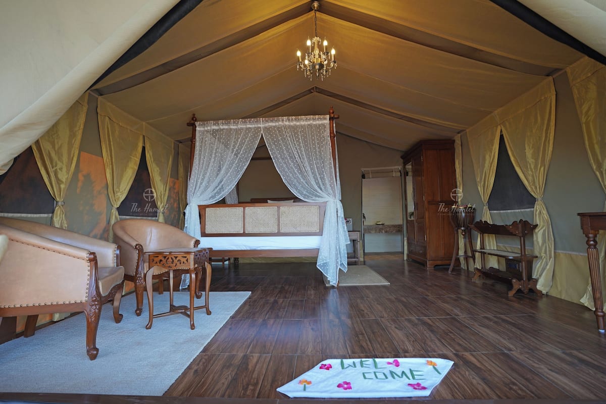 Una habitación con tienda, una cama, un sofá, un candelabro y un tapete de bienvenida.