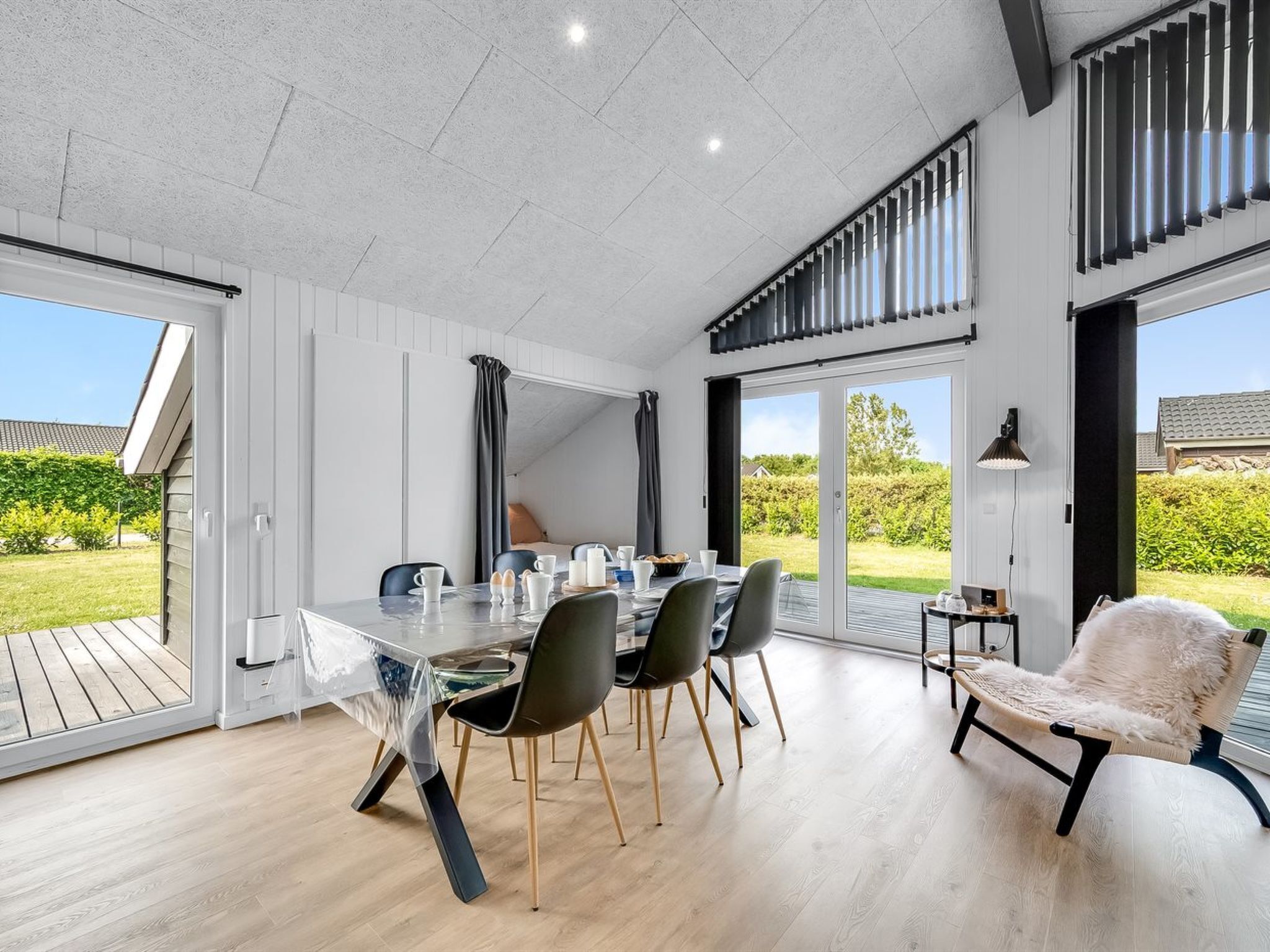 A modern dining area with a glass table, black chairs, and a white chair with a fur throw.