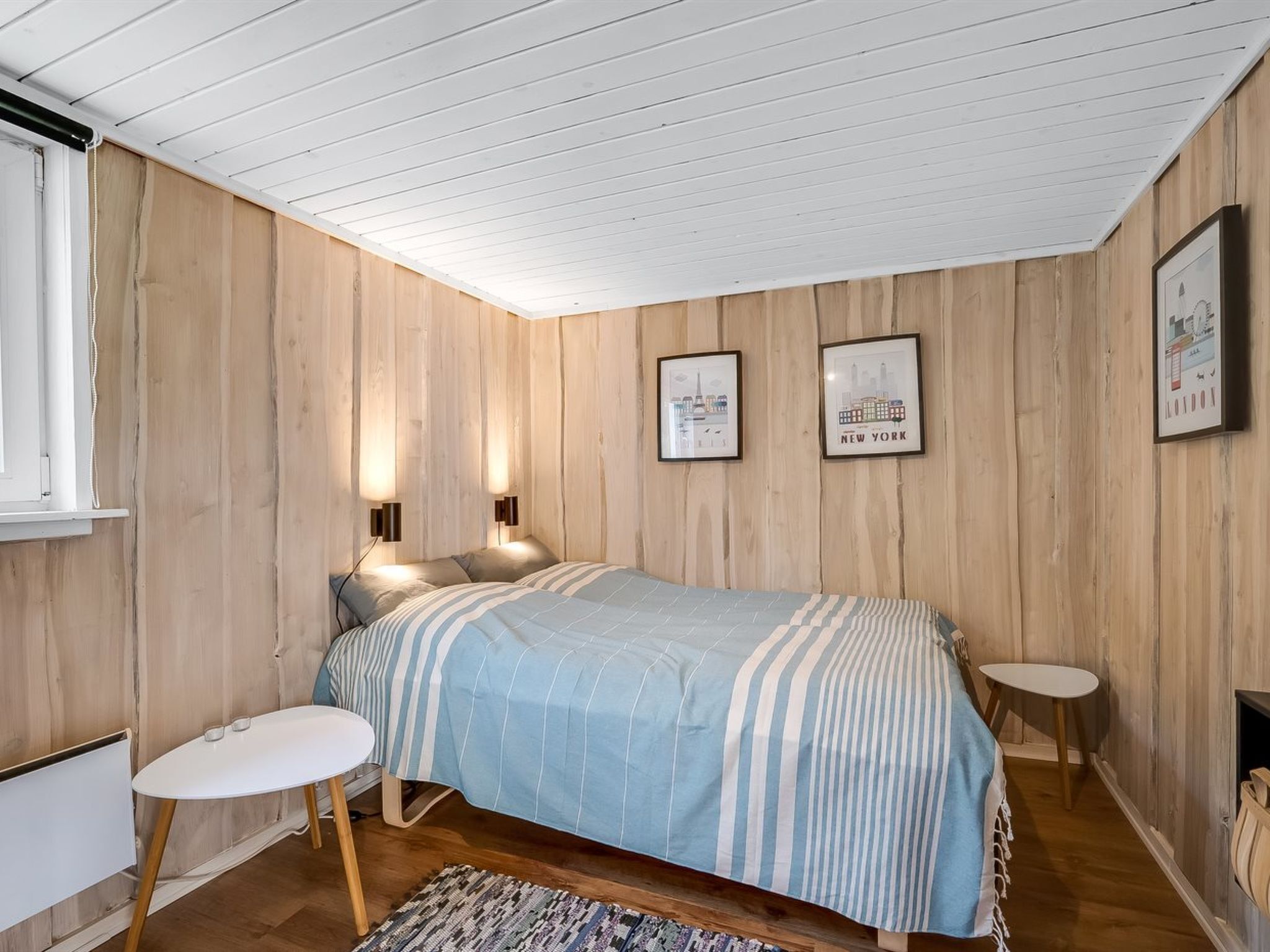 Une chambre à coucher avec un lit, deux tables de chevet, un radiateur et des tableaux encadrés accrochés au mur.