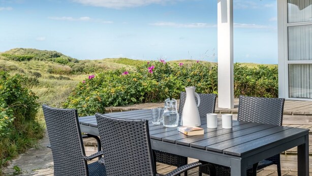 Une terrasse extérieure avec une table et des chaises, un vase blanc et un livre.