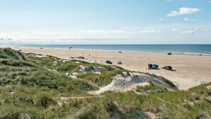 Une plage avec des dunes, des véhicules et un ciel dégagé.