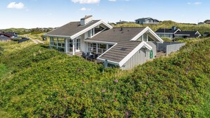 Une maison située sur la côte, dotée d’un toit en pente, de grandes fenêtres et d’une terrasse.
