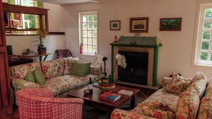 A cozy living room with floral-patterned sofas, a checkered armchair, a fireplace, and a bookshelf. - Casa do Bosque Campos do Jordão (Campos do Jordão)