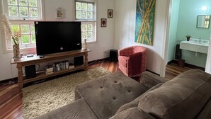 A living room with a large flat-screen TV on a wooden stand, a red armchair, and a beige rug. - Casa do Bosque Campos do Jordão (Campos do Jordão)