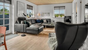 A modern living room with a wooden ceiling, large windows, a grey sofa, a coffee table, and a TV.
