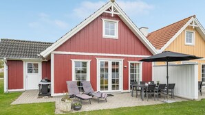 Une maison rouge avec un toit en tuiles, une terrasse avec des meubles d’extérieur et un barbecue.