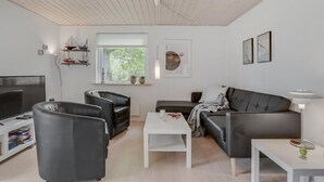 Una sala de estar moderna con televisor, sillones de cuero, un sofá, una mesa de centro y obras de arte en las paredes.