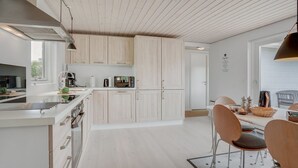Una cocina moderna con armarios de madera clara, una isla central y un comedor con sillas y una mesa.