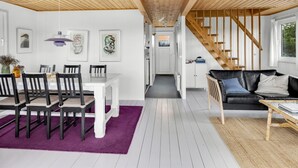 Amplia sala de estar con techo de madera, una mesa de comedor con sillas, un sofá de cuero negro y una escalera.