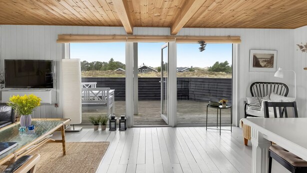 Un interior moderno con techo de madera, un televisor, una mesa de comedor y vistas a través de grandes puertas de vidrio.