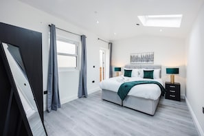 Relax in a spacious room with a large bed, flat-screen TV, and natural light pouring in through the skylight.