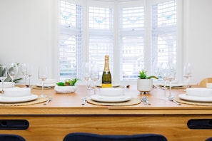 Enjoy meals in this dining area with a long table set for a meal, featuring white plates, wine glasses, and a bottle of wine.