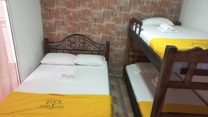 A room with two bunk beds, each with a wooden headboard and white bedding. A yellow towel is placed on the lower bunk, and a folded towel is on the upper bunk. The room has a brick wall and a wooden floor. - Apartment 1cl2 in the Walled Center With Aircon (Cartagena)