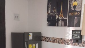 A compact kitchen with a refrigerator, a dining table, and chairs. There are wall-mounted pictures depicting Paris landmarks and a 'Save Water Drink Beer' sign. - Apartment 1cl2 in the Walled Center With Aircon (Cartagena)