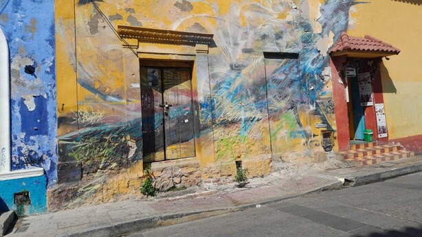 A building with a yellow facade, a black door, and a small entrance with a red roof. - Apartment 1cl2 in the Walled Center With Aircon (Cartagena)
