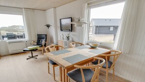 A dining area with a wooden table and chairs, a television mounted on the wall, and a view of the outside through large windows. - "Terhi" - 200m from the sea by Interhome (Fanø)