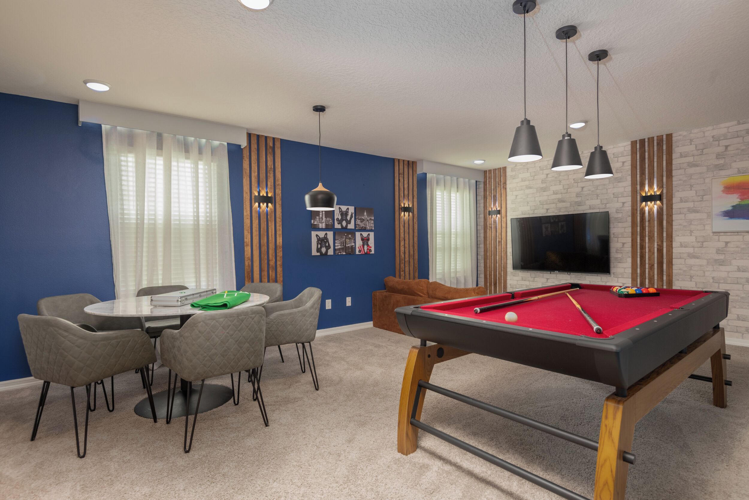 A room with a pool table, a TV mounted on the wall, and a dining area with chairs and a table.