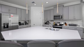 A modern kitchen with grey cabinets, a stainless steel refrigerator, a microwave, and a large island with a sink.