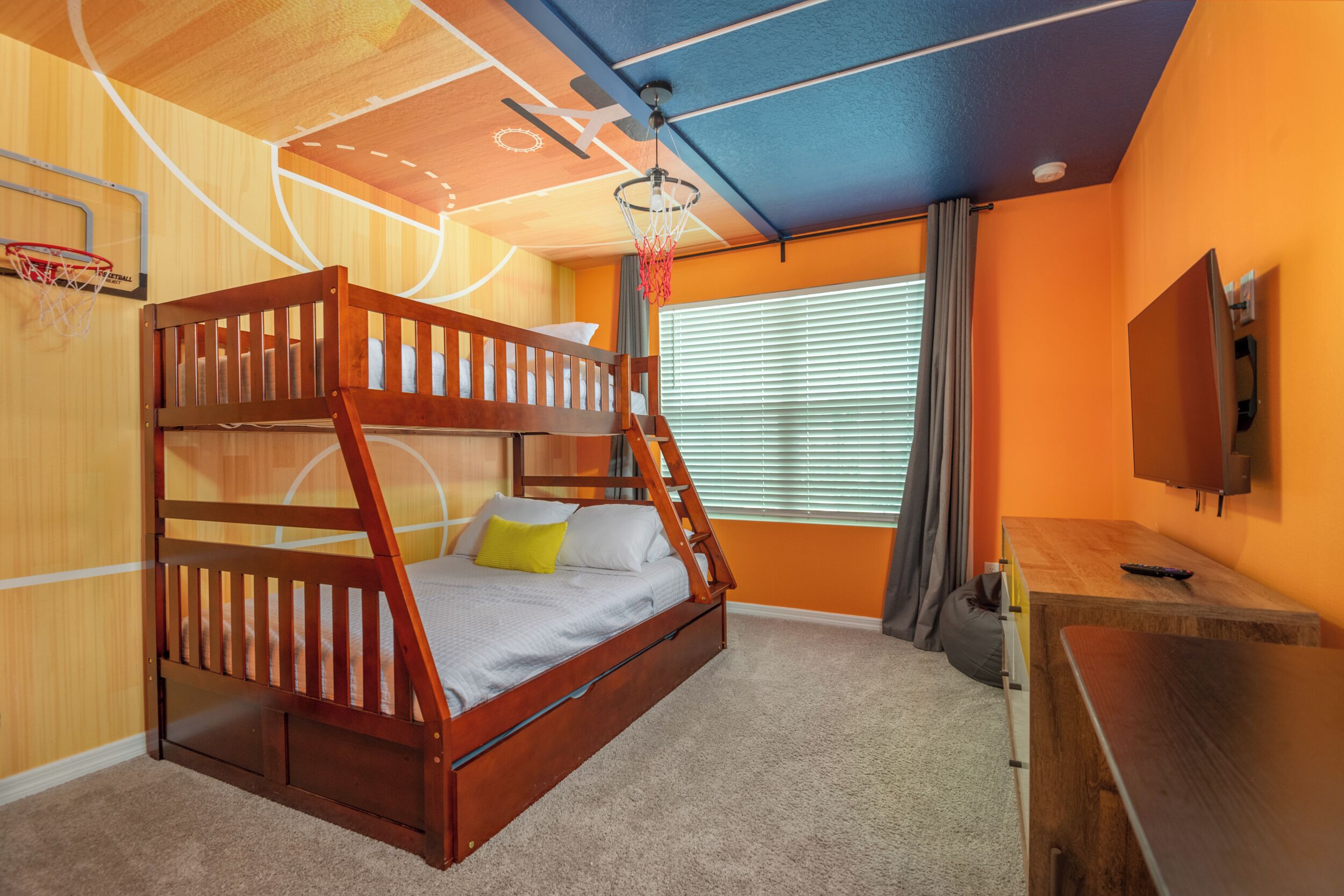 A bunk bed with a basketball hoop, a desk, and a TV in a room with orange walls and a ceiling fan.