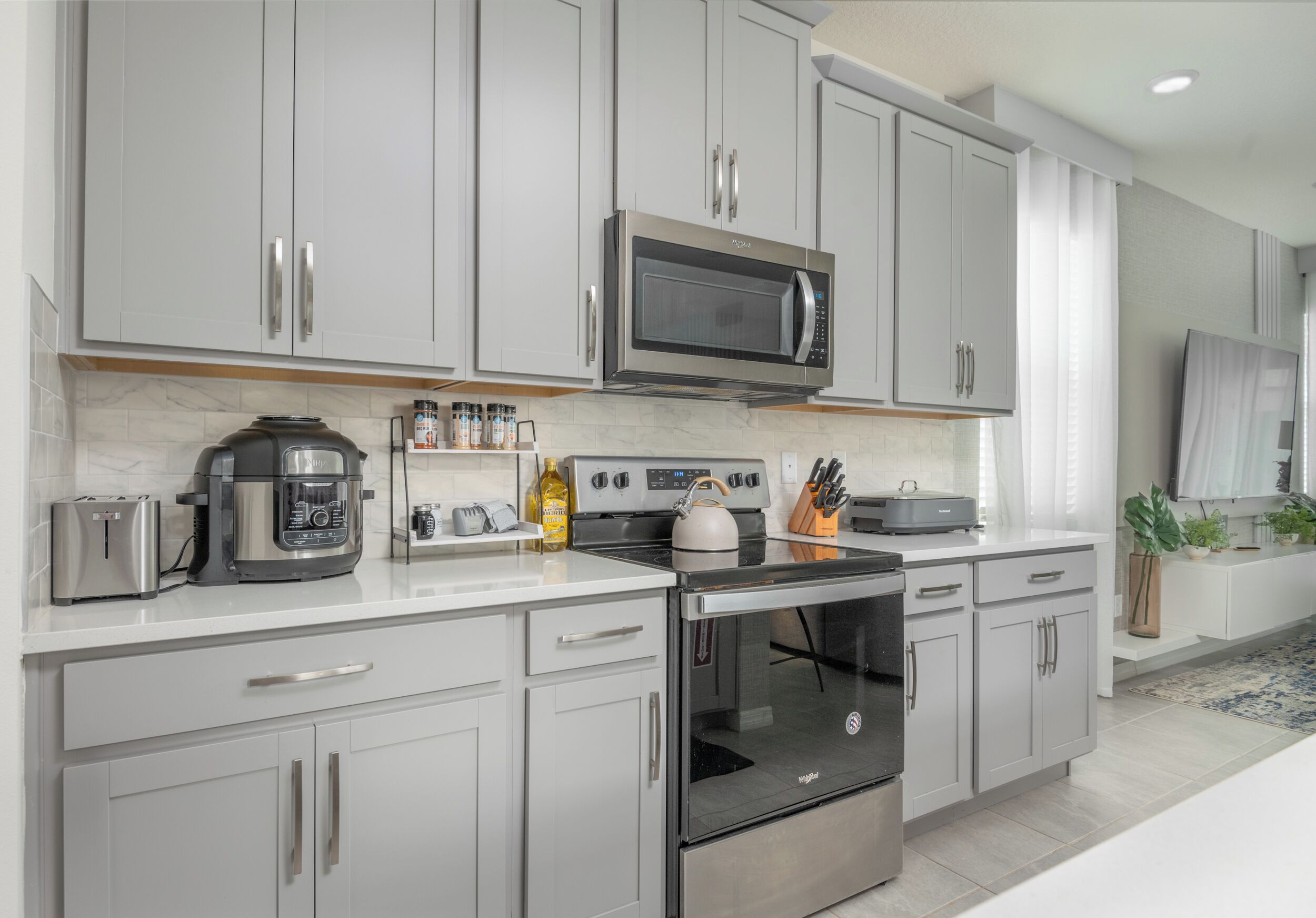A modern kitchen with stainless steel appliances, grey cabinetry, and a built-in oven.