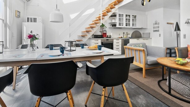 Eine moderne Küche mit weißen Schränken, einer Holztreppe und einem Essbereich mit schwarzen Stühlen.