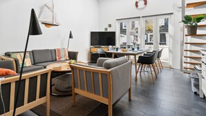 Ein modernes Wohnzimmer mit Sofa, Couchtisch und Fernseher, ein Essbereich mit Stühlen und Tisch sowie eine Treppe mit Pflanze.