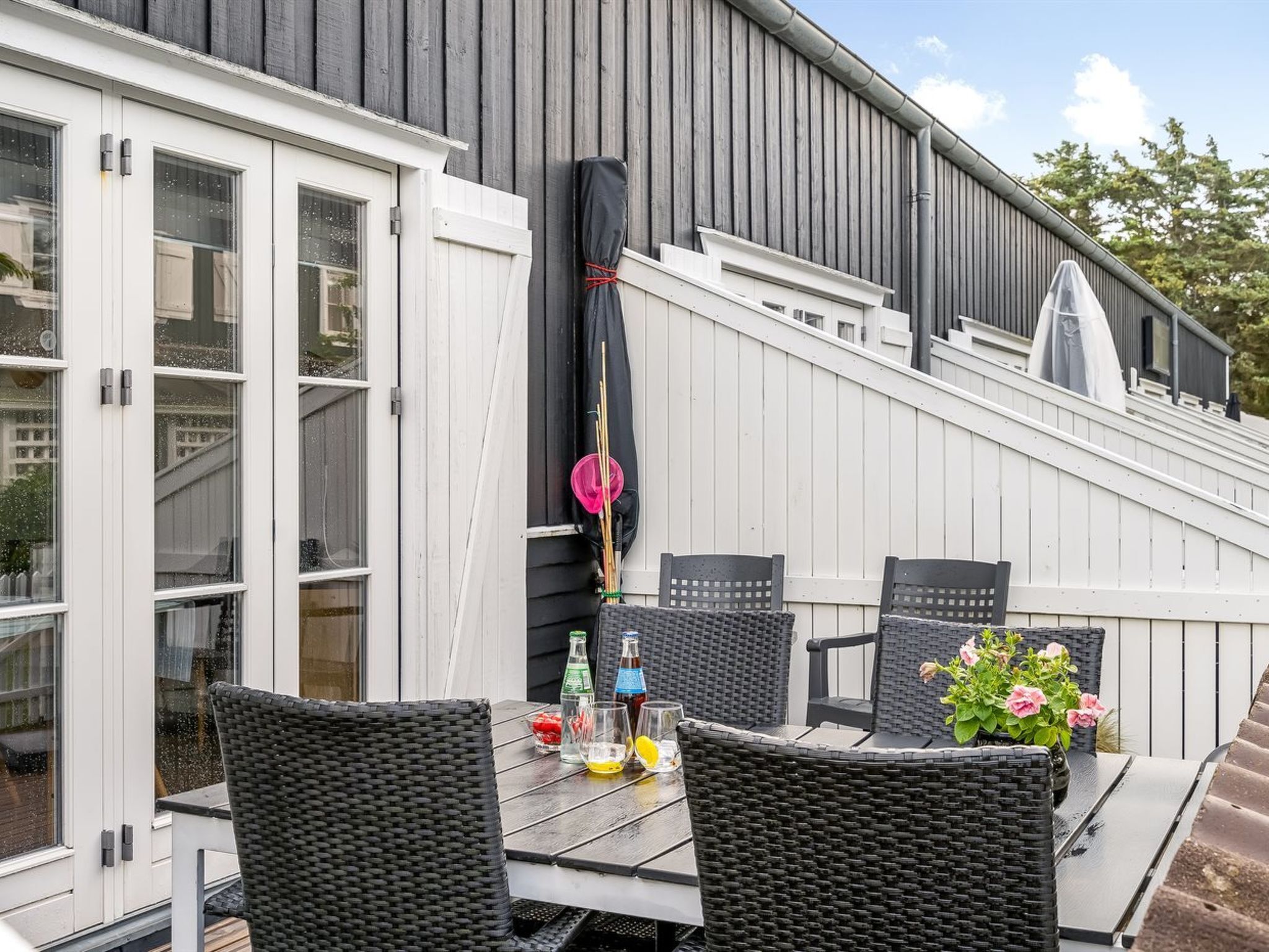 Eine Außenpatio mit Tisch und Stühlen, einem überdachten Bereich und einem Gebäude mit großen Fenstern und einer Holzfassade.