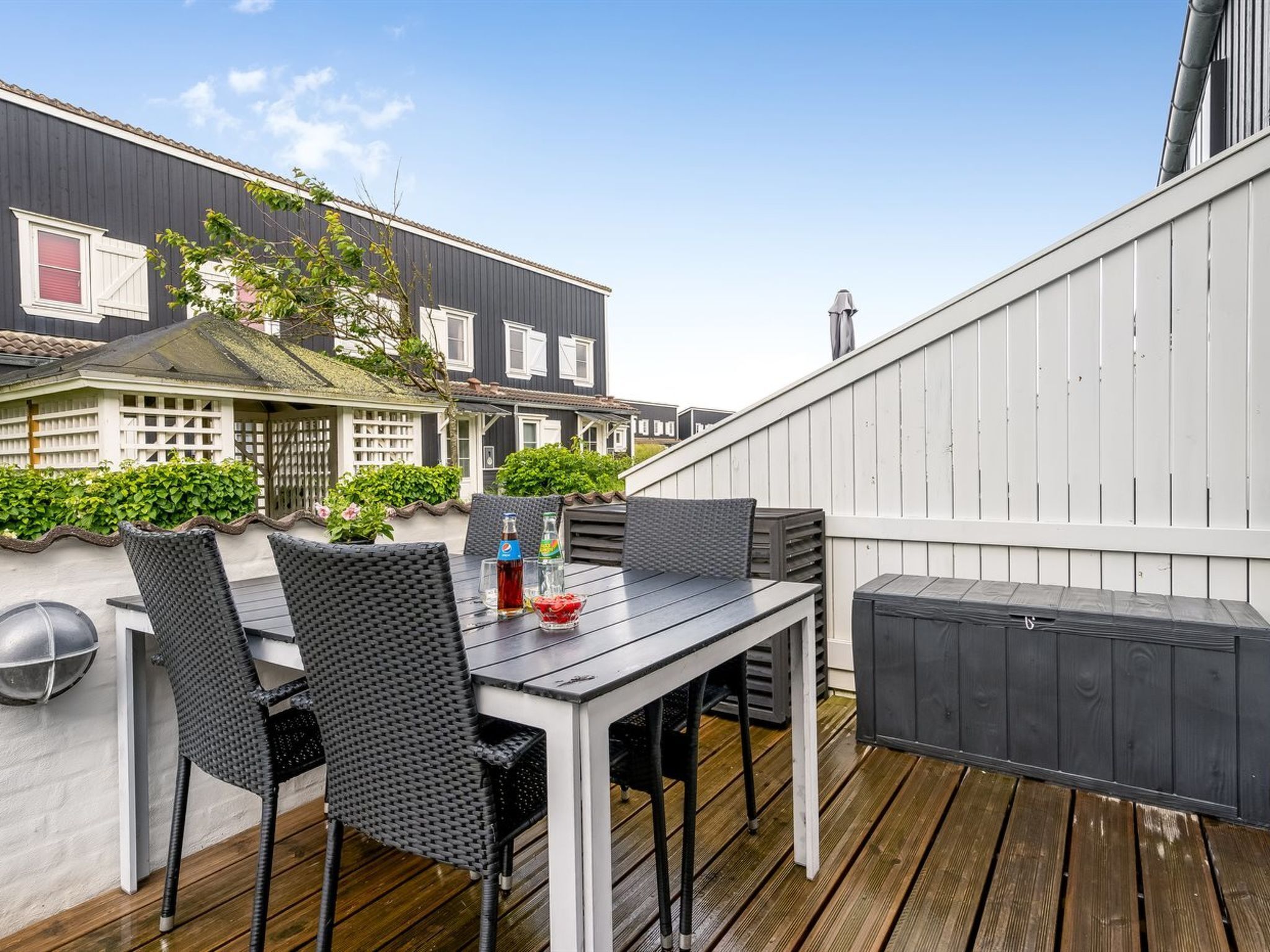 An outdoor patio with a table and chairs, a grill, and a white fence.